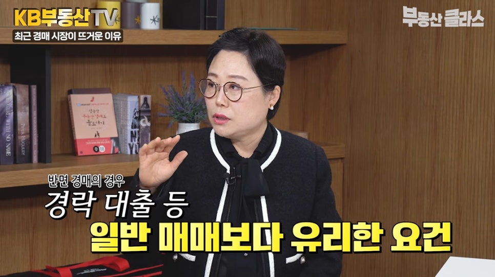 '이선미 대표가 경매의 장점을 설명하는 장면'입니다. 화면 하단에 '반면 경매의 경우 경락 대출 등 일반 매매보다 유리한 요건'이라는 노란색 자막이 표시되어 경매의 금융적 이점을 강조하고 있습니다.