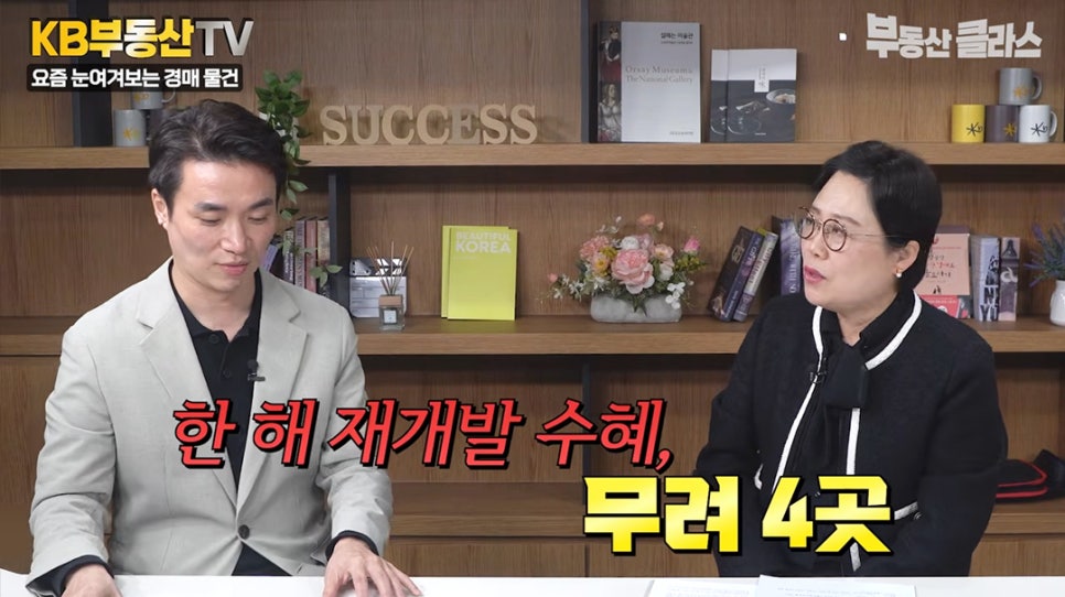 '두 명의 출연진이 대화를 나누는 모습'입니다. '요즘 눈여겨보는 경매 물건'이라는 주제 아래, '한 해 재개발 수혜, 무려 4곳'이라는 자막이 떠 있어 재개발 지역 내 경매 물건의 가치를 시사하고 있습니다.