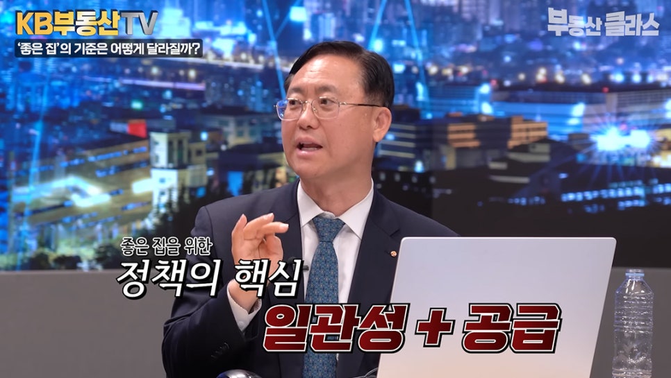 '전문가가 손동작을 하며 정책의 방향성을 제안하는 모습'이다. 화면에는 좋은 집을 위한 정책의 핵심으로 '일관성 + 공급'이라는 키워드가 굵고 선명한 자막으로 강조되어 있다.