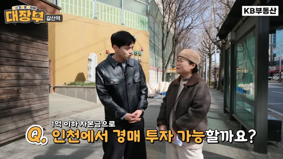 야외에서 남녀 출연자가 '1억 이하 자본금으로 인천에서 경매 투자가 가능할지' 질문을 던지며 '대화를 나누는 방송 화면'입니다.