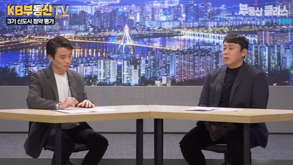 '야경을 배경으로 한 스튜디오에서 두 남성이 대화를 이어가는 모습'입니다. 좌측 상단에는 '3기 신도시 청약 평가'라는 소제목이 있어 해당 주제에 대한 분석이 진행되고 있음을 보여줍니다.