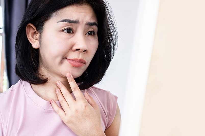한 여성이 거울을 보며 불만족스러운 표정을 짓고 있다.