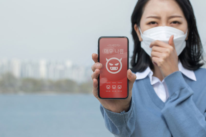 강 주변에서 한 여성이 '스마트폰'으로 '미세먼지' 매우 나쁨 표시를 보여주고 있다.