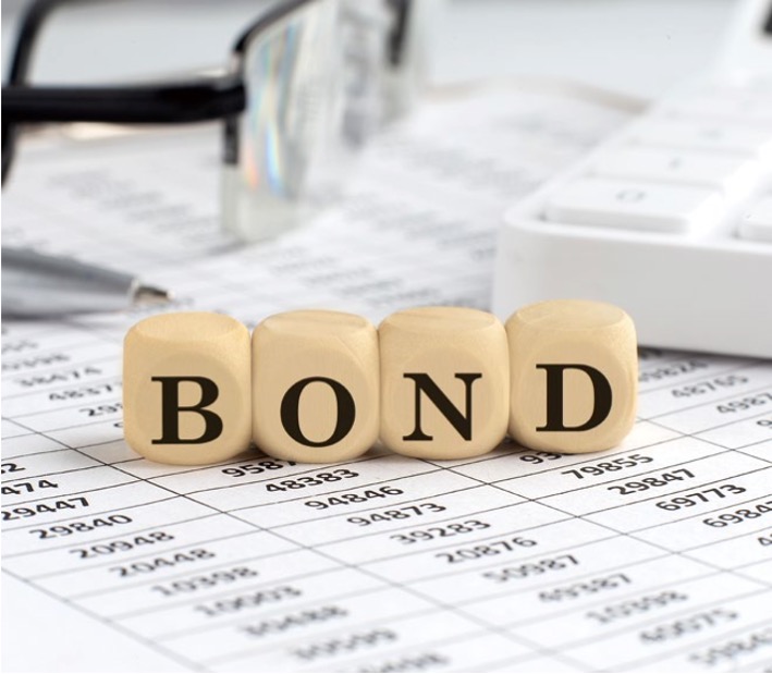 여러 숫자를 가득 담은 표위에 안경, 계산기 그리고 'BOND'라고 쓰여있는 나무 블록이 위치해있다.