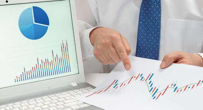 정장 차림의 사람이 모니터 화면과 '종이 차트'를 가리키는 모습이다.