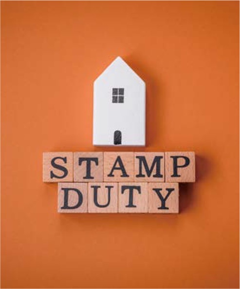 '주황색 배경 위에 흰색 집 모형 아래 STAMP DUTY라고 쓰여 있는 나무 블록들'이 놓여 있는 모습입니다.