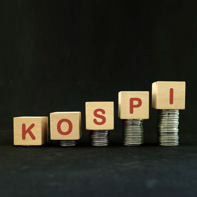 나무 블록에 'KOSPI'라고 적혀있다. 오른쪽으로 갈수록 더 높은 동전들이 쌓여있다.