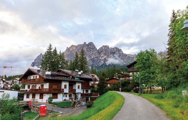 '구름이 내려앉은 거대한 암벽 산 아래로 고즈넉한 목조 가옥들과 완만하게 굽은 산책로가 어우러져 평화로운 산악 마을의 일상'을 보여준다.