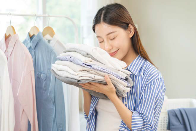 잘 정리된 '빨래감'에 얼굴을 묻고 기분 좋은 표정을 짓는 여성의 사진이다.