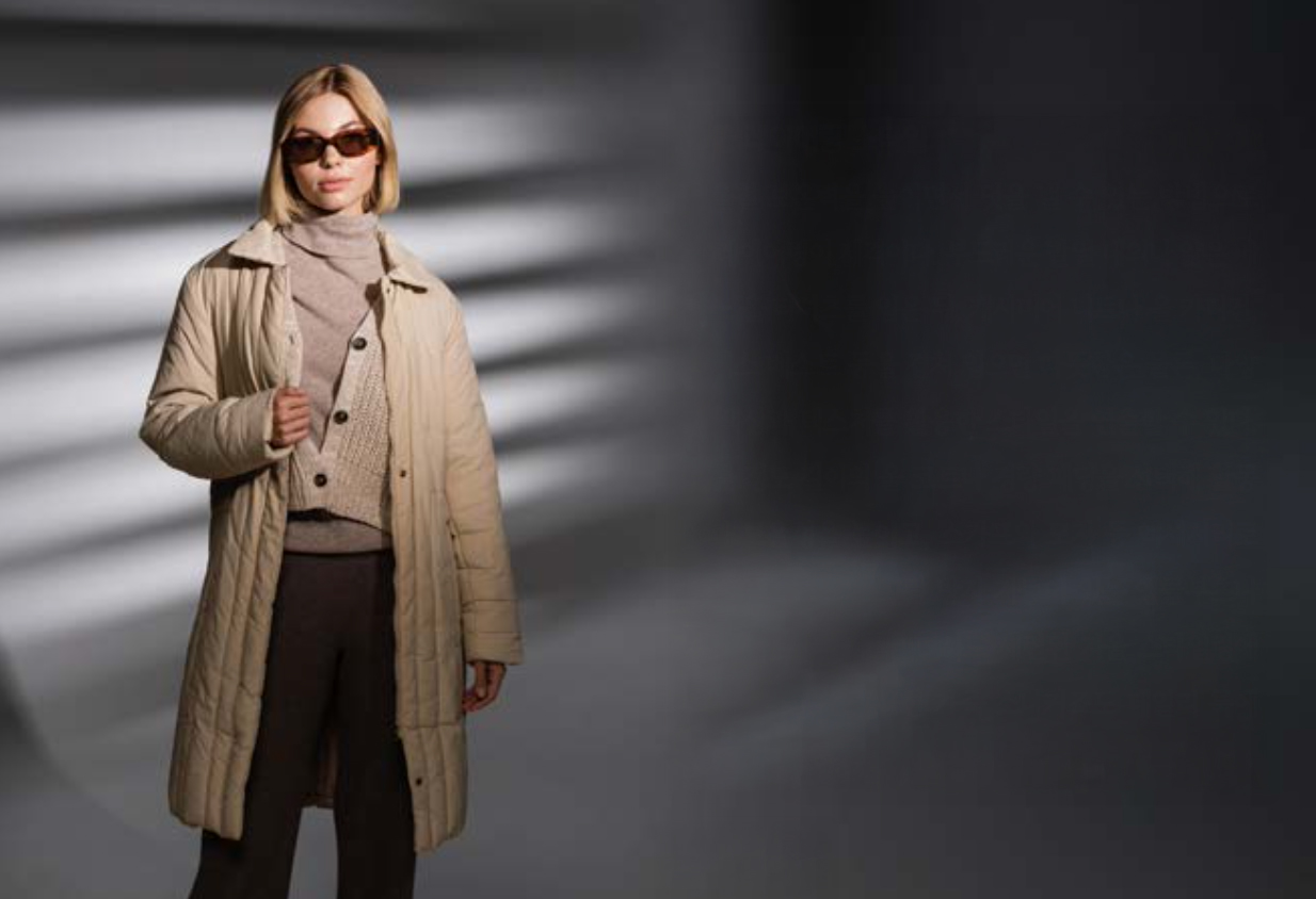 어두운 배경 앞에 선 여자 모델이 겨울철 보온력을 높일 수 있게 캐시미어 니트와 울 카디건, 롱패딩을 입고 레이어링 스타일을 보여주고 있다.