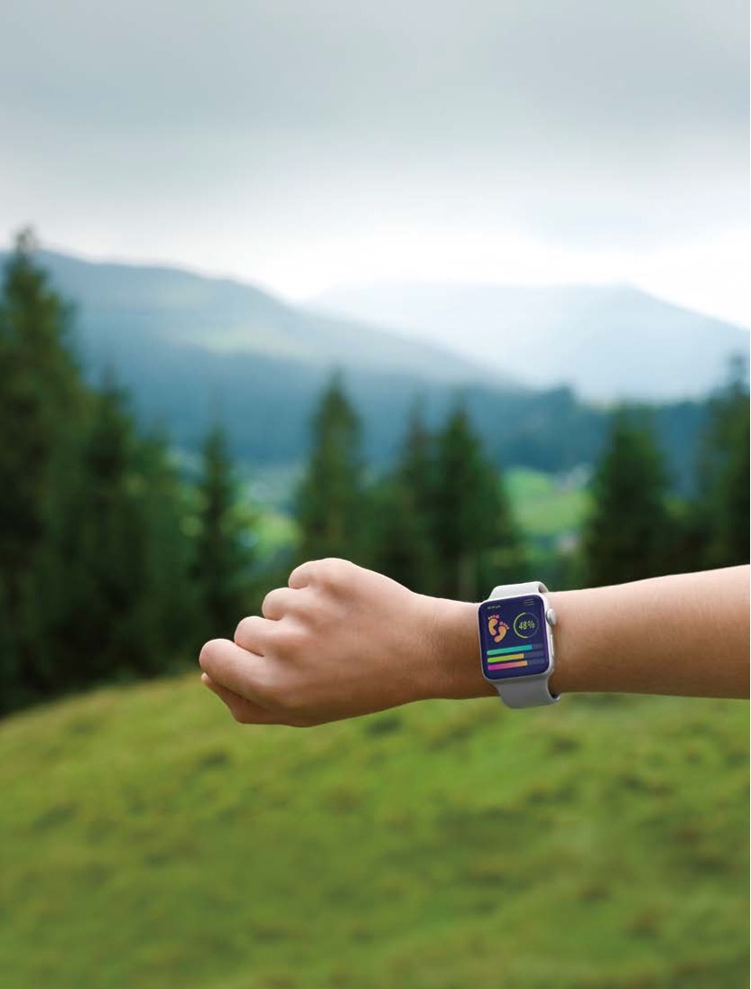 '자연 속 초원 배경에서 손목에 스마트워치를 착용하고 활동량을 확인하는 모습'이다.