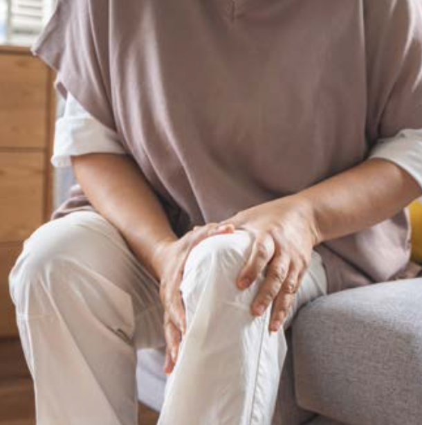 의자에 앉아있는 사람이 무릎에 통증을 느끼는 듯한 모습으로 무릎을 두 손으로 감싸 쥐고 있다.