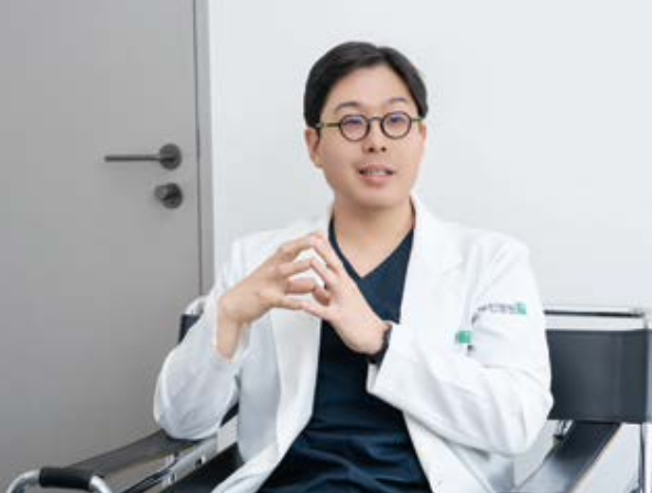 남자 원장님이 검은색 의자에 앉아서 양손을 모으고 질문에 대한 대답을 하고 있다.