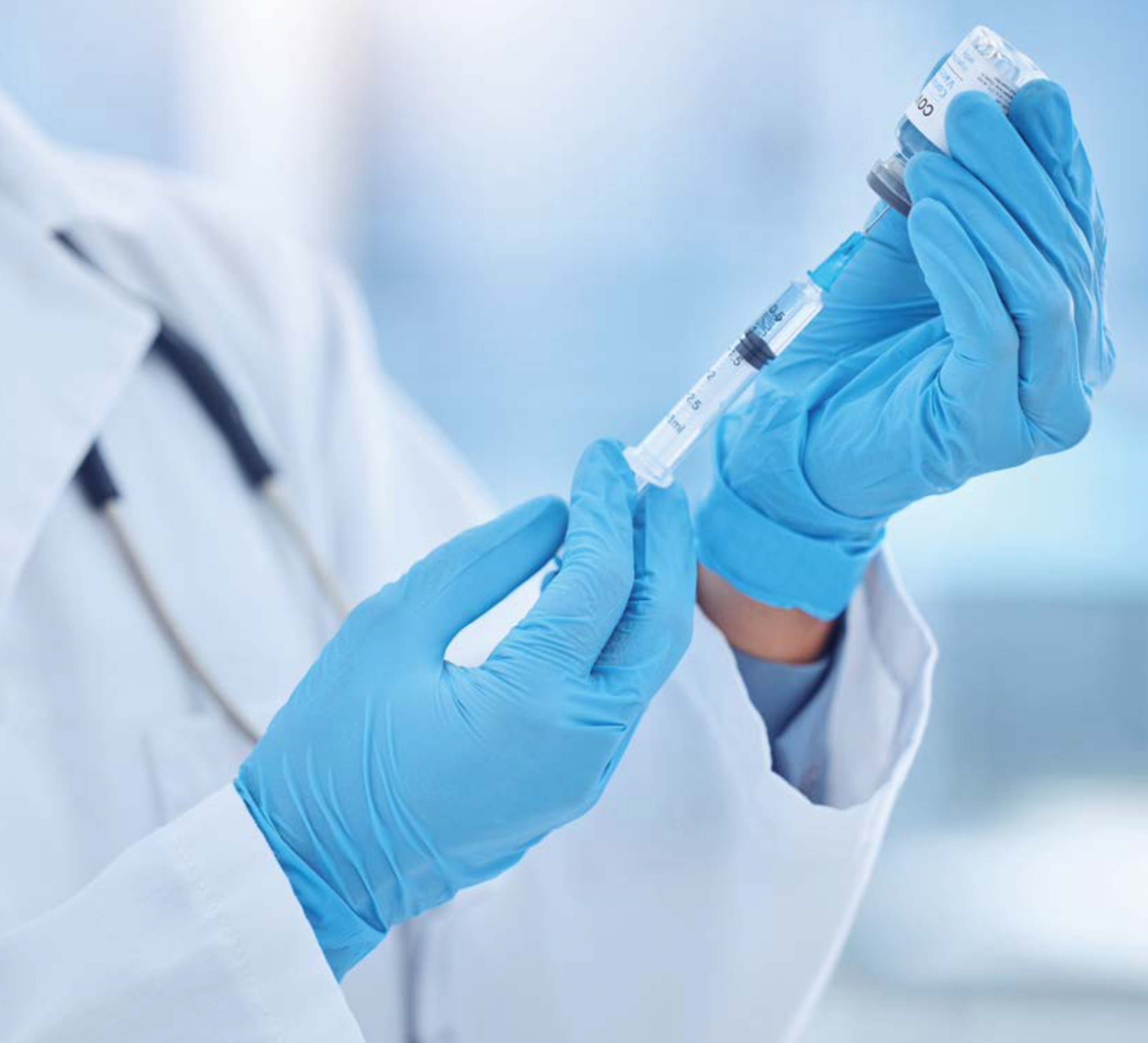 파란색 의료용 장갑을 낀 ‘의료진이 주사기에 백신 액체를 신중하게 옮겨 담고 있는 모습’입니다.