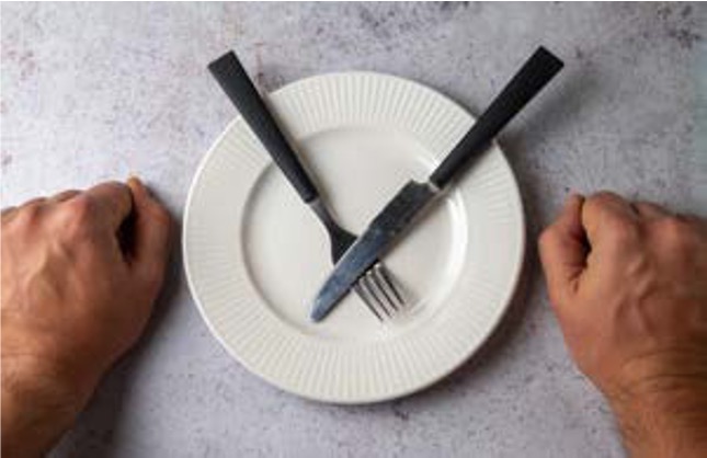 빈 접시 위에 '포크와 나이프가 X자로 놓여' 있고, '양옆에 주먹 쥔 두 손'이 놓인 탑뷰 이미지이다.