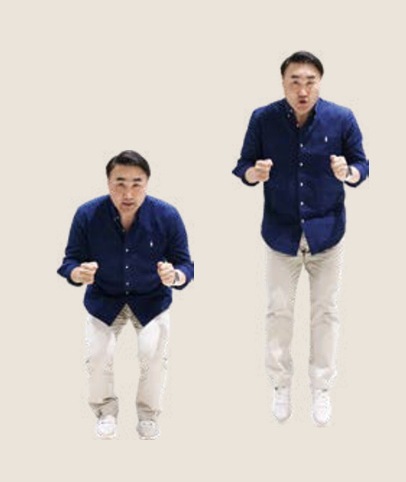 '남색 셔츠와 베이지색 바지를 입은 남성이 제자리에서 무릎을 굽혔다 힘차게 위로 점프'하고 있다.