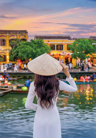 '전통 의상'을 입은 사람이 등불이 켜진 호이안의 강변을 바라보는 모습이다.