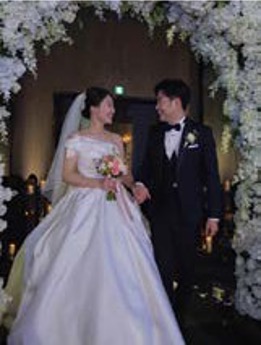 '꽃 아치 아래의 신랑 신부가 서로를 마주 보며 웃고 있고 주변에 분홍 꽃잎'이 흩날린다. 영상 편집 중 후반 이미지이다.