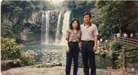 '폭포를 배경으로 중년 부부가 나란히 서서 정면을 응시하며 찍은 오래된 느낌의 사진'이다.