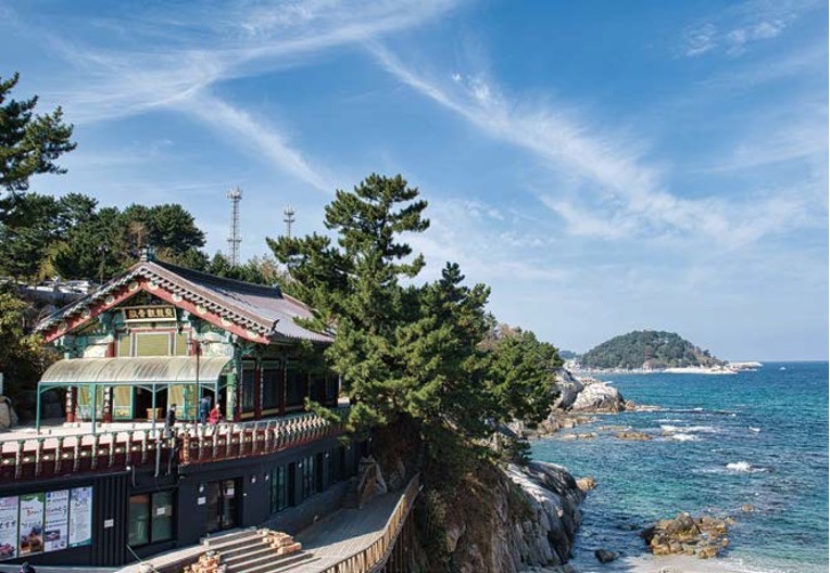 '맑은 하늘과 푸른 바다가 펼쳐진 해안가 절벽 위에 한국 전통 양식의 사찰' 건물이 자리 잡고 있다.