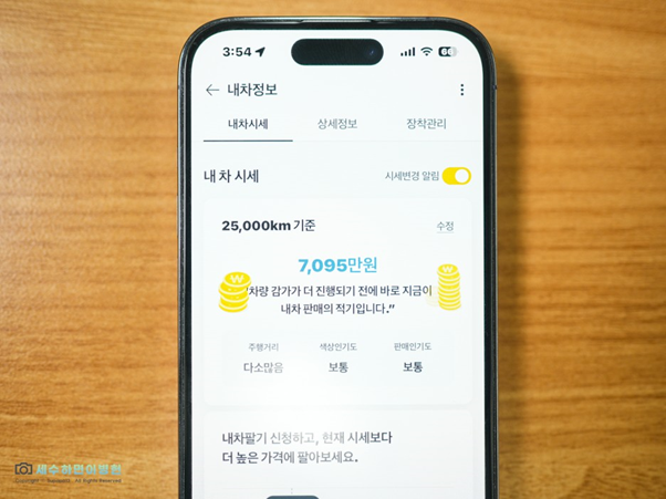 나무 책상 위 스마트폰, 'KB차차차' 앱을 통해  중고차 감가  주 원인과 검색 모델의 현 상태를 파악할 수 있는 서비스 소개.