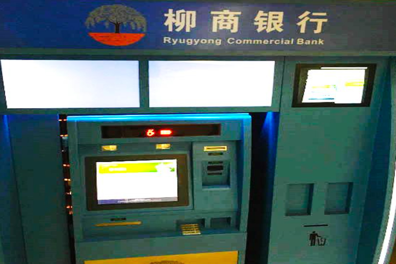 평양의 '류경상업은행에서 사용하는 ATM' 기기이다. 녹색 기기 전면에 화면과 버튼이 배치돼 있으며, 실내에 설치된 단일 ATM 모습이 보인다.