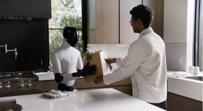 가정 내 주방 환경에서 인간과 상호작용하는 휴머노이드 로봇 '피규어 01(Figure 01)'의 모습입니다. 로봇이 사람에게 종이봉투를 건네주는 장면을 통해 일상 속 피지컬 AI의 활용 예시를 보여줍니다.