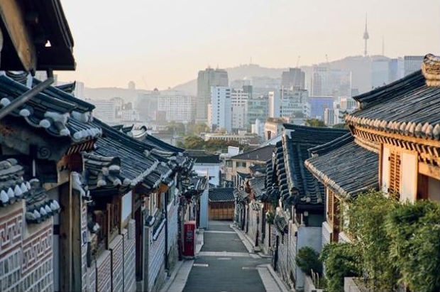 '기와지붕과 담장이 이어지는 한옥 골목 너머로 현대식 고층 건물과 도심 풍경이 펼쳐진 사진'이다. 전통 주거 공간과 현대 도시 건축이 한 화면에 공존하여 한국의 압축적 근대화를 시각적으로 보여준다.