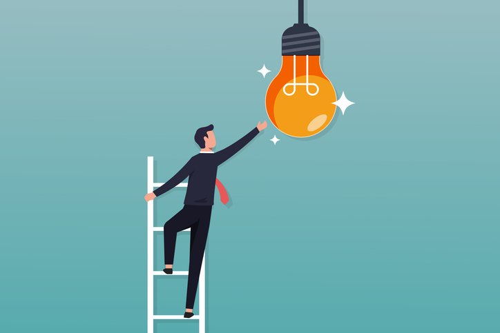 사다리에 올라탄 남자가 천장에 매달린 전구쪽으로 손을 뻗고 있다.