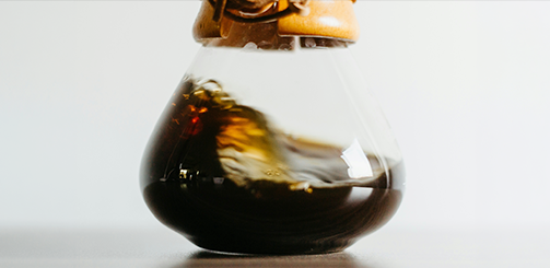 'RELAX'라고 적힌 카페 유리창 너머 따뜻한 조명 아래 사람들의 모습과 함께 '디카페인, 새로운 취향이 되다'라는 문구가 포함된 이미지.