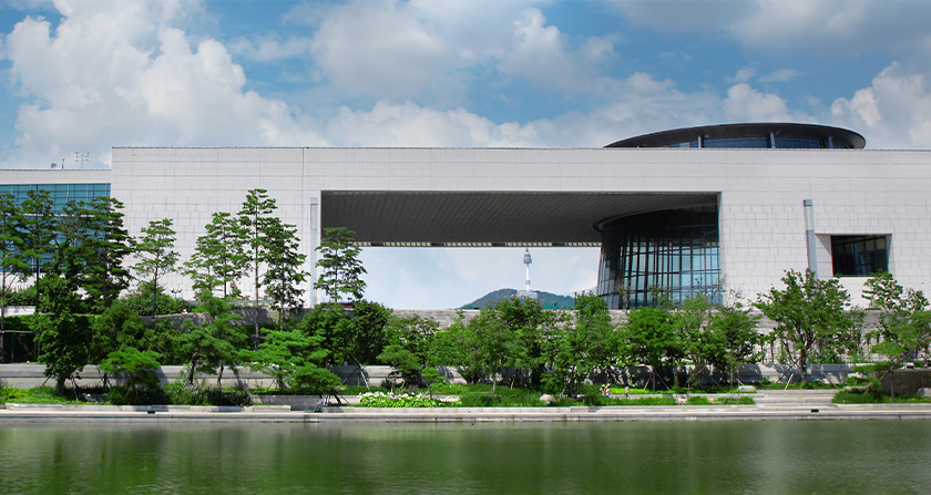 박물관 전시실의 미니멀한 화이트 테이블 위에 놓인 다양한 크기와 모양의 한국 전통 청화백자들. 배경에는 2027년 유료 전환 안내와 박캉스 코스 추천 텍스트가 포함됨