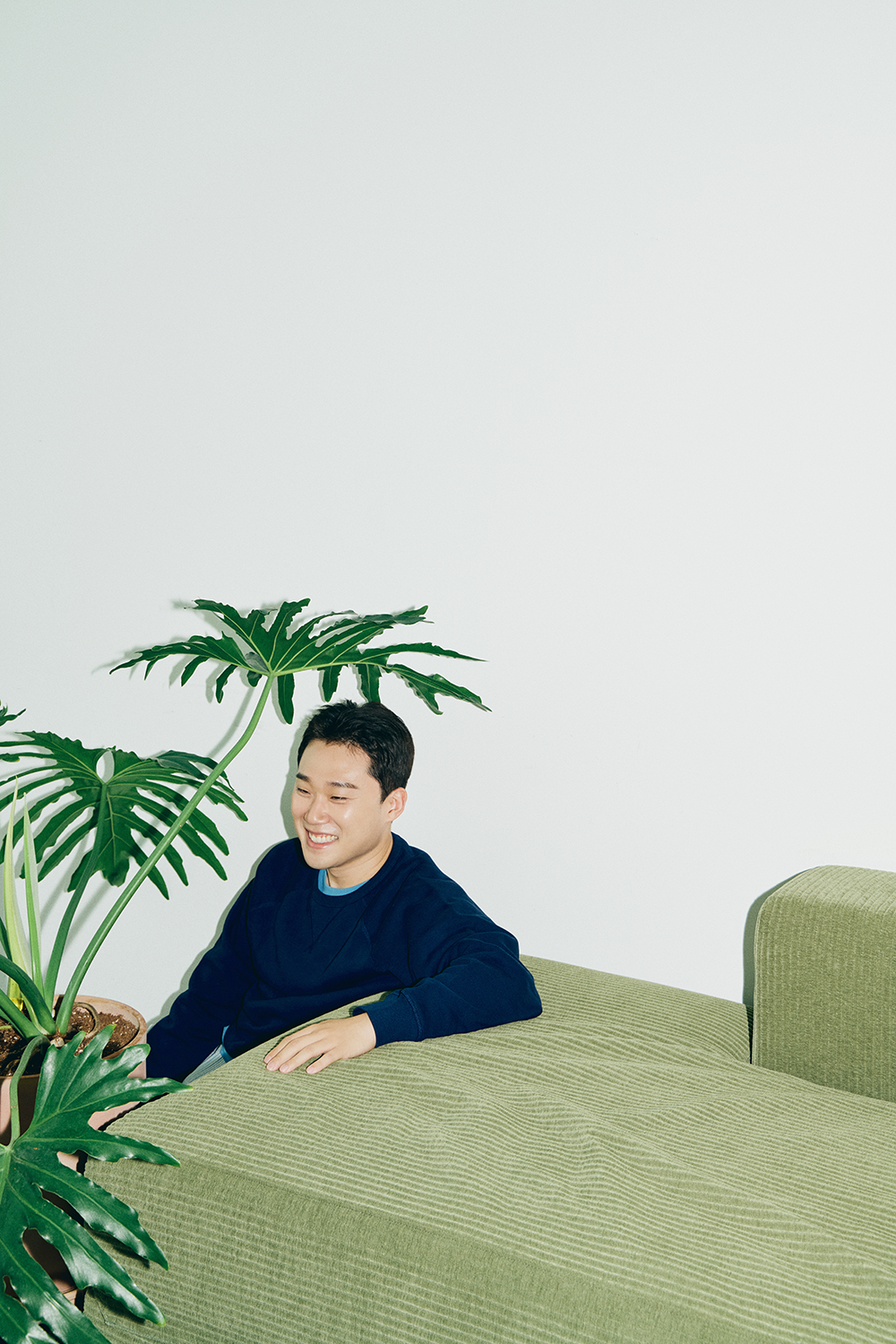 바닥에 앉아 초록 소파에 몸을 기대고 웃고 있는 자취남