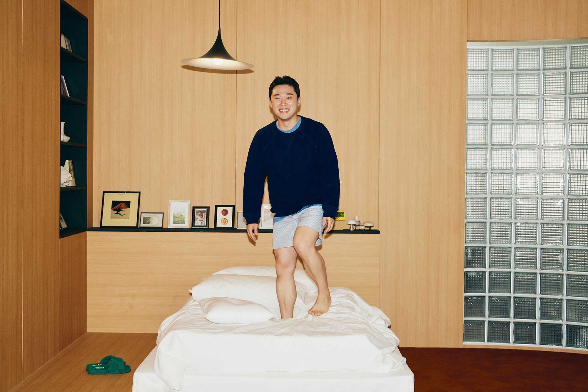 편안한 반바지 차림과 신나는 표정으로 침대 위를 뛰고 있는 자취남