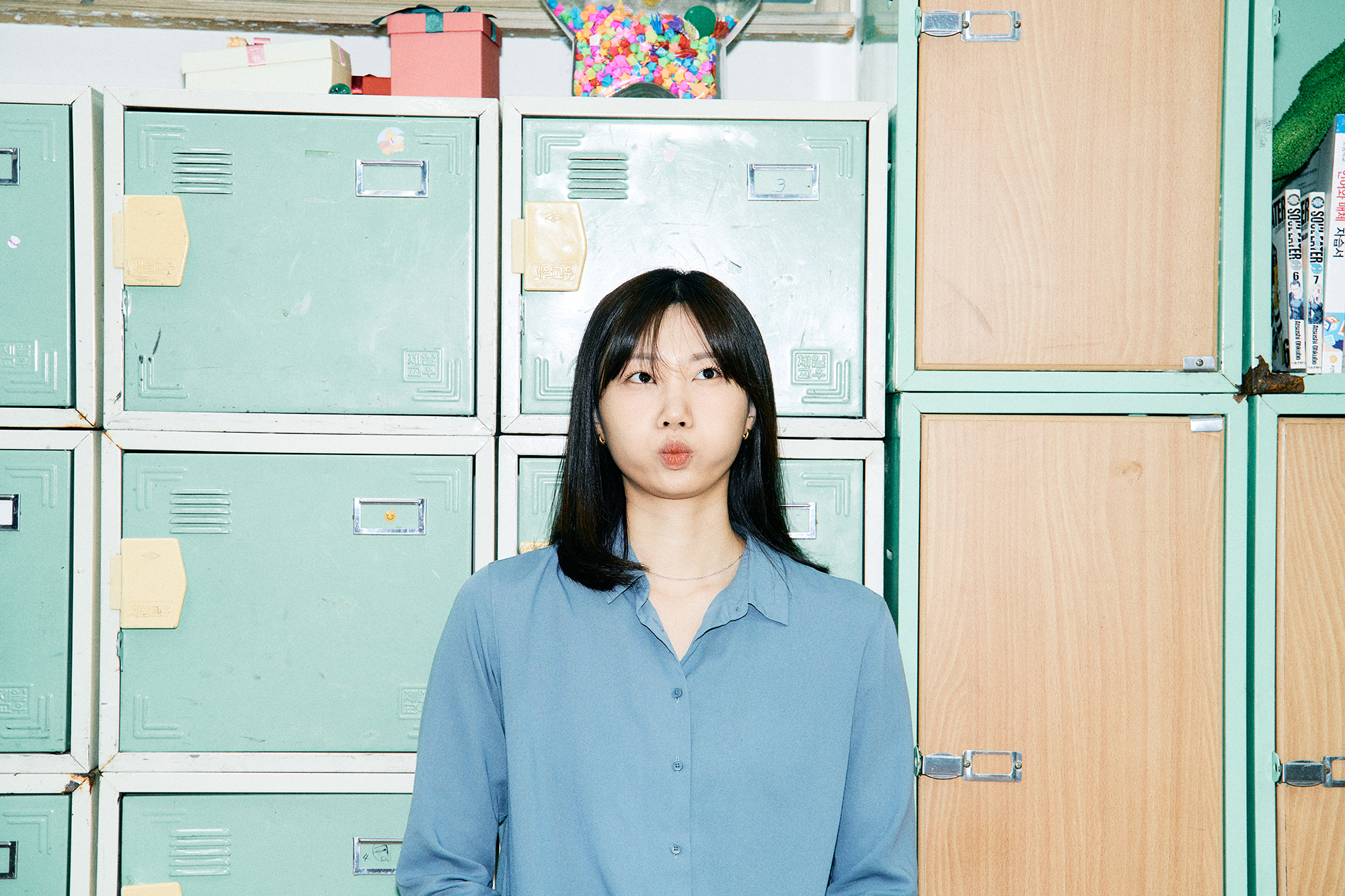 옛 초등학교 교실을 배경으로 사물함 앞에 서서 볼에 바람을 채우고 익살스러운 표정을 짓고 있는 슈카월드PD 니니