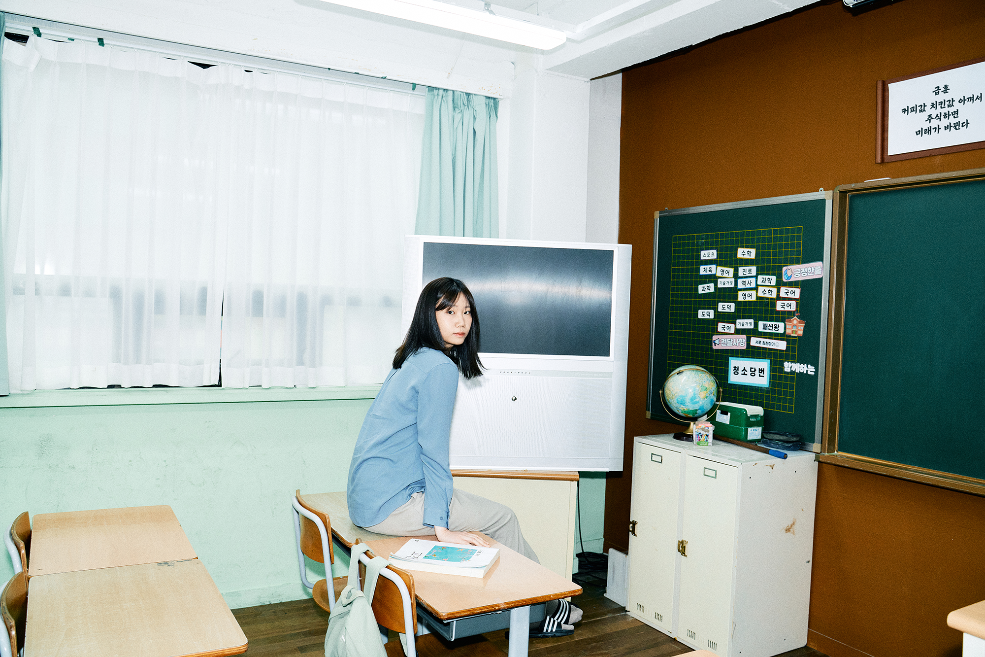 옛 초등학교 교실 책상에 앉아 있는 뒤를 돌아보고 있는 슈카월드PD 니니