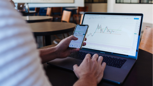 스마트폰과 노트북으로 동시에 주식 차트를 보는 사람의 모습. 주식 리딩방 가짜 홈트레이딩 시스템을 표현한다.
