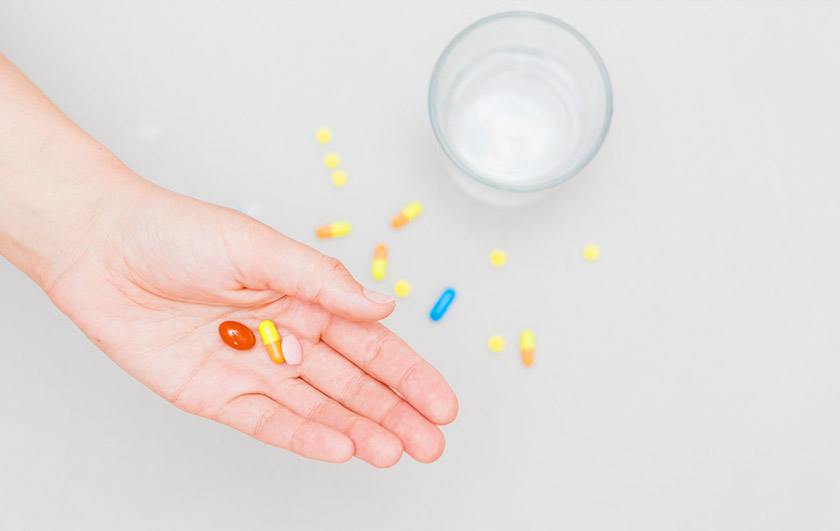 물이 담긴 유리잔이 놓여 있고 영양제를 손바닥 위에 올려놓은 모습. 