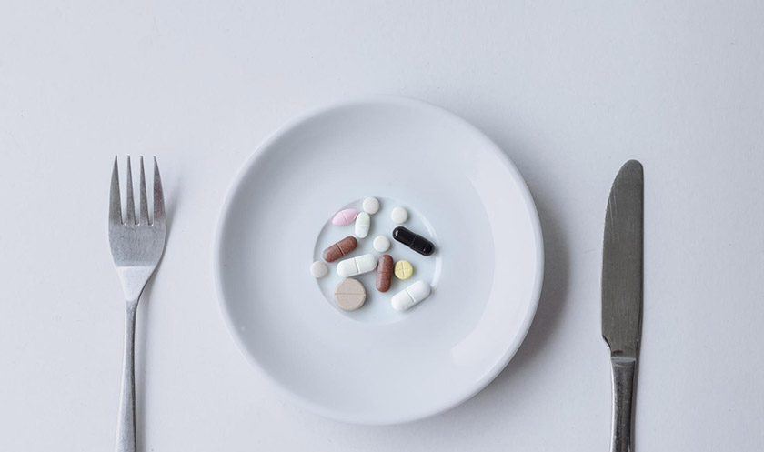 그릇 위에 영양제 여러 알이 놓여 있고, 양쪽에 포크와 나이프가 있다.