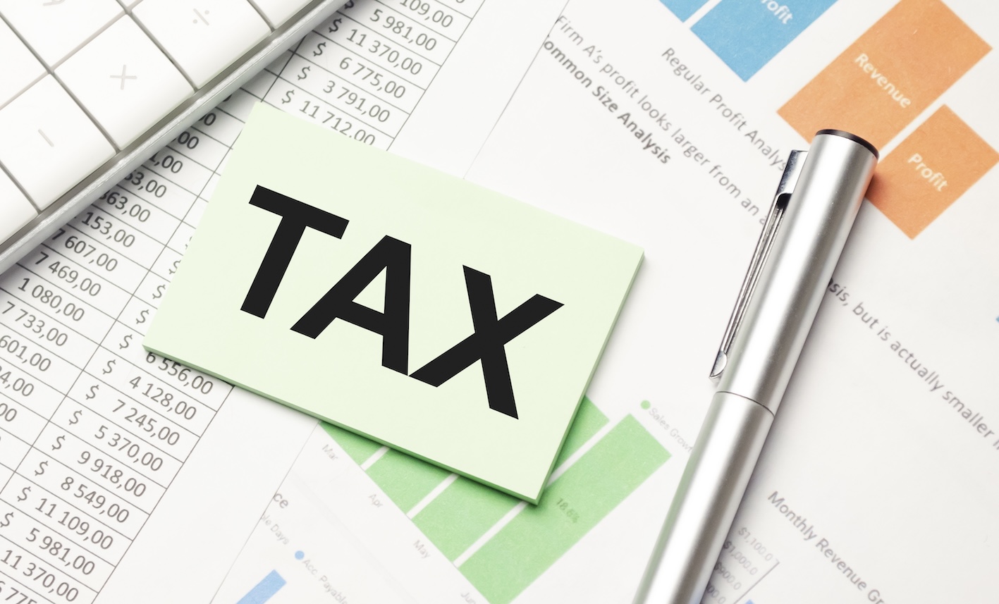 종이 위에 포스트잇과 펜이 놓여있고. 포스트잇에 TAX라는 글씨가 적혀있다.