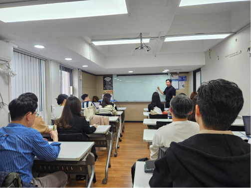 경제살롱 모임 사진. 강의실에서 한 사람이 나와 칠판을 가리키고 있고 나머지 인원은 경제 공부를 위해 강연 내용에 집중하는 모습.