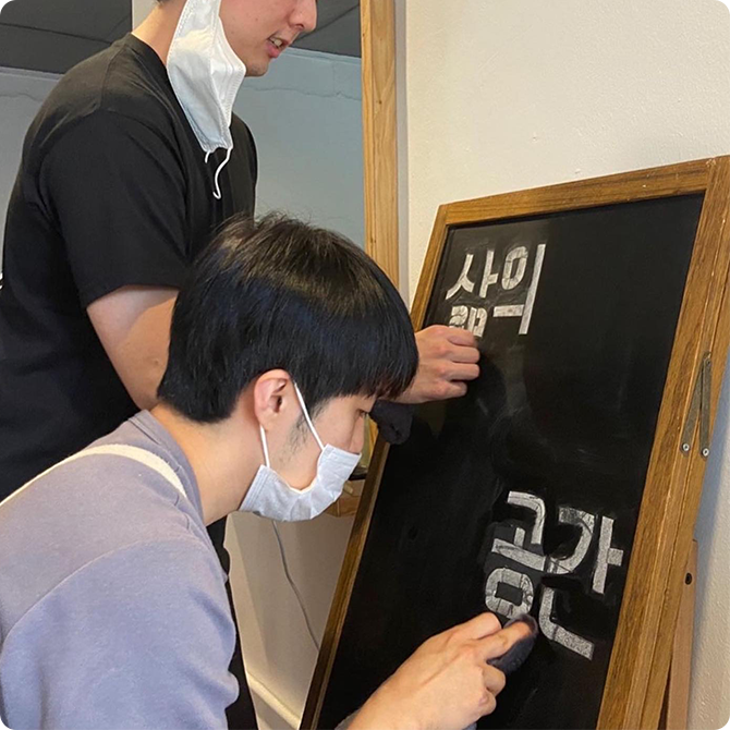 미용실의 입간판을 제작하고 있는 두 남성의 모습이다.